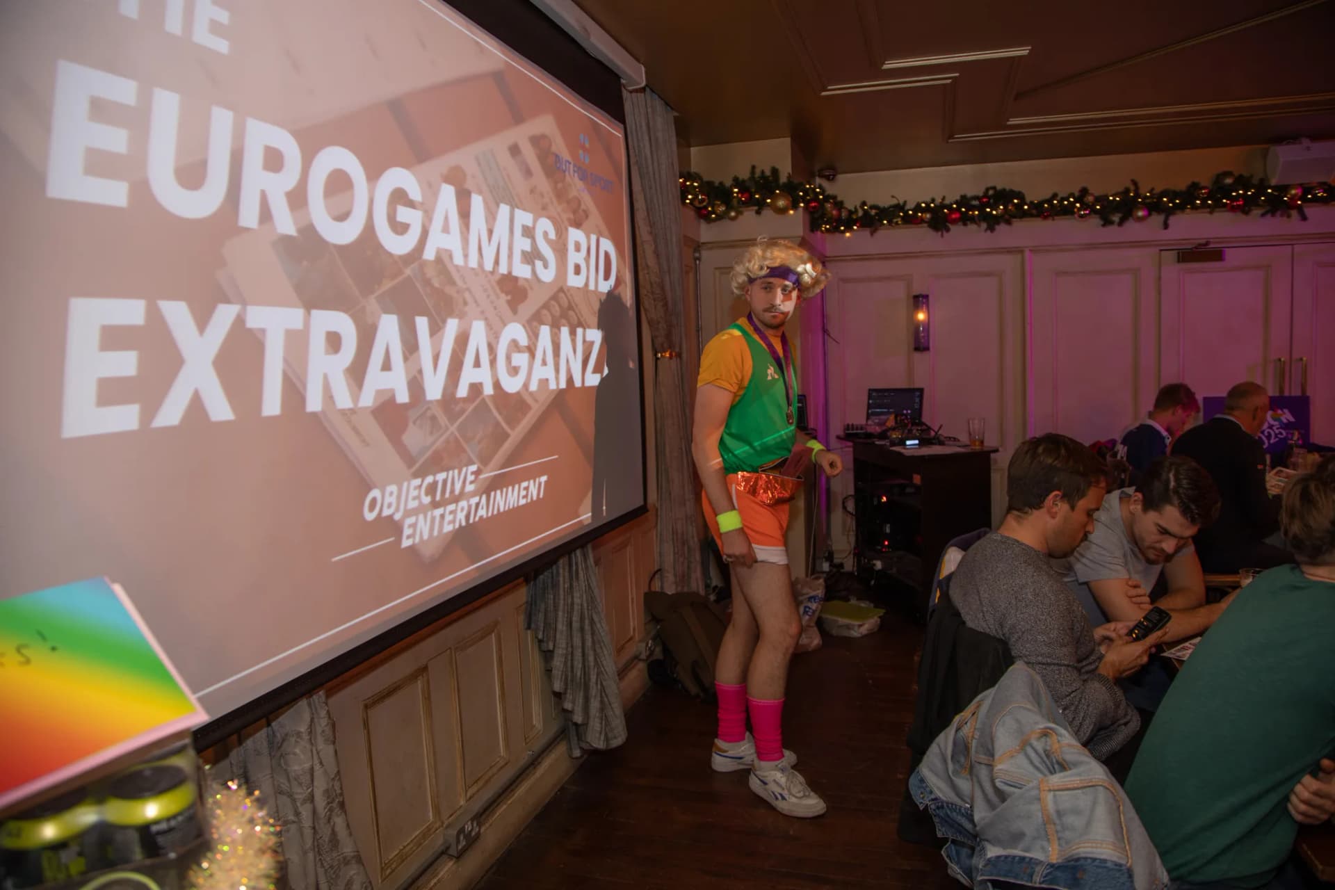 Costumed host beside the EuroGames Bid Extravaganza screen.